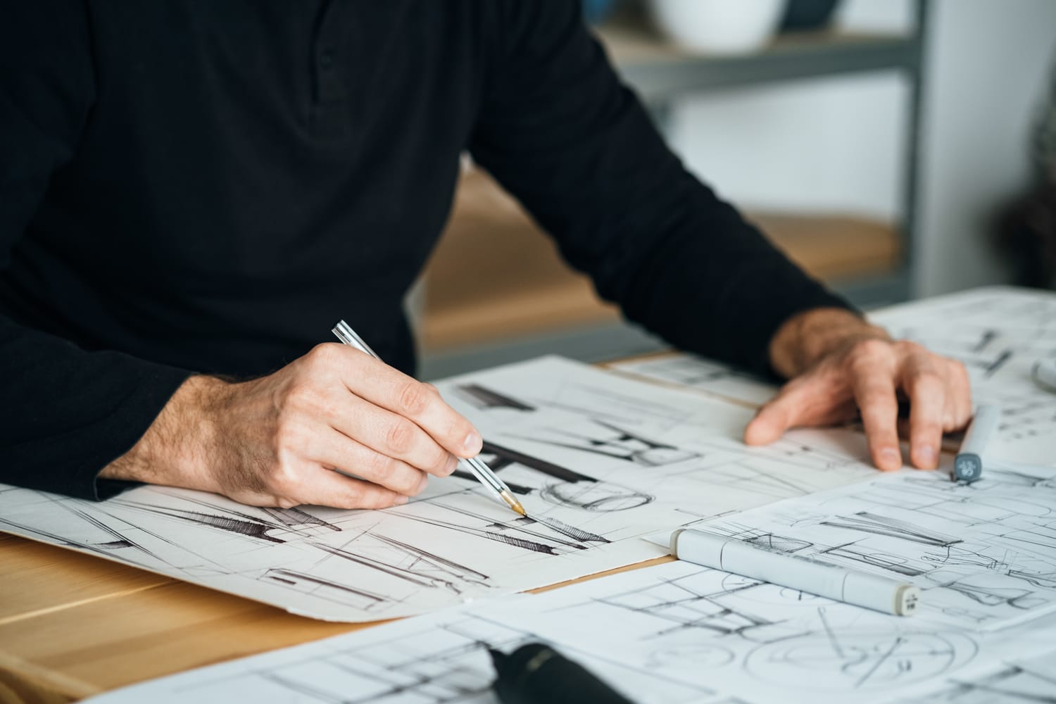 A designer's hands sketching over architectural blueprints